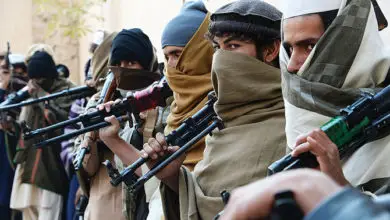 Taliban fighters holding weapons stand in a queue