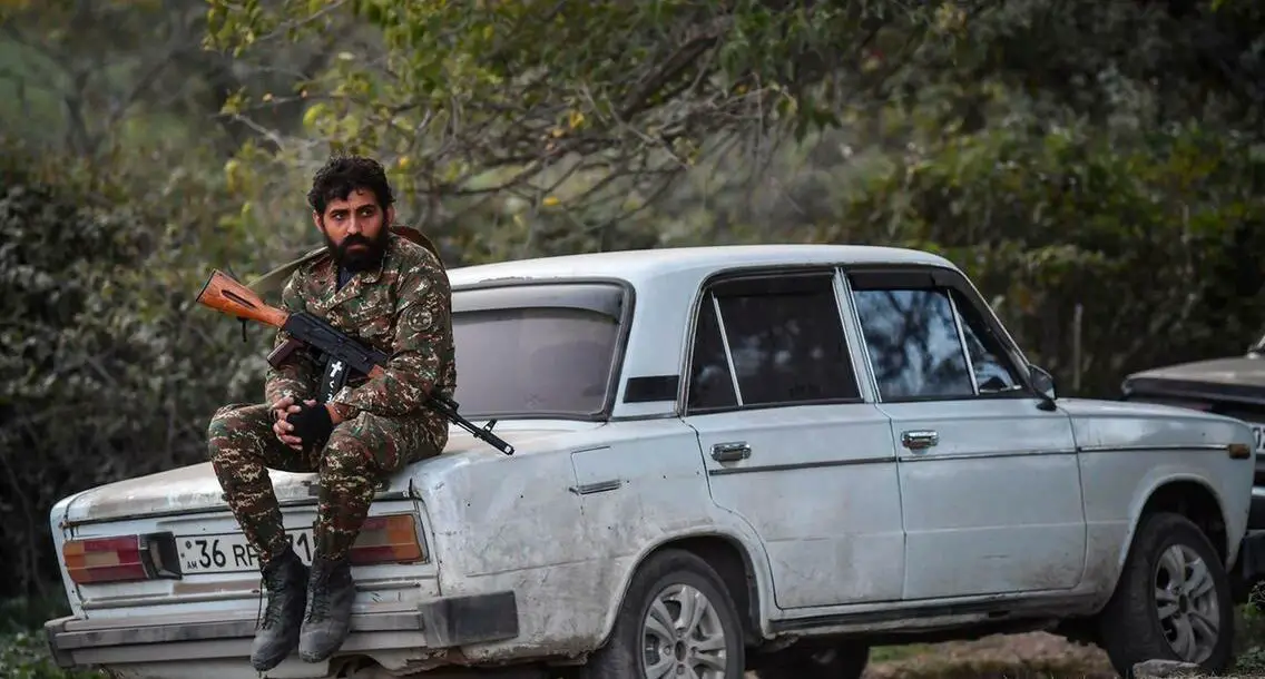 A volunteer fighter sits on a car as cannons fire nearby