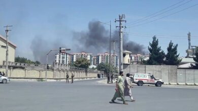 Afghan men walk on a road as smoke rises from the site of an attack in Kabul on 1 July 2019.