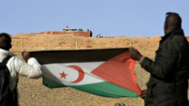Saharawi men hold up a Polisario Front flag in the Al-Mahbes area near Moroccan soldiers guarding the wall separating the Polisario controlled Western Sahara from Morocco on February 3, 2017.