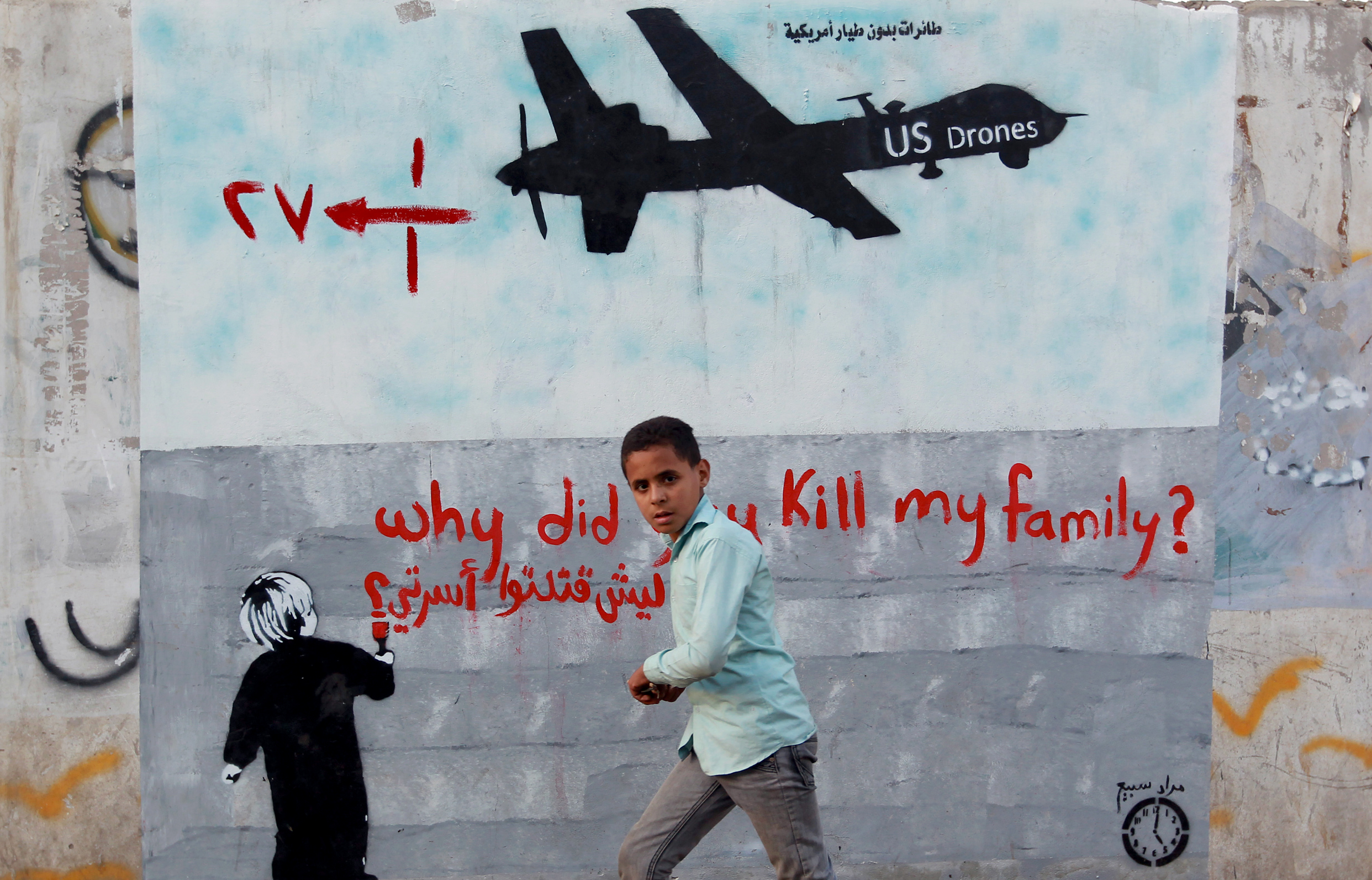 A Yemeni boy walks past a mural depicting a US drone and reading "Why did you kill my family" on December 13, 2013 in the capital Sana