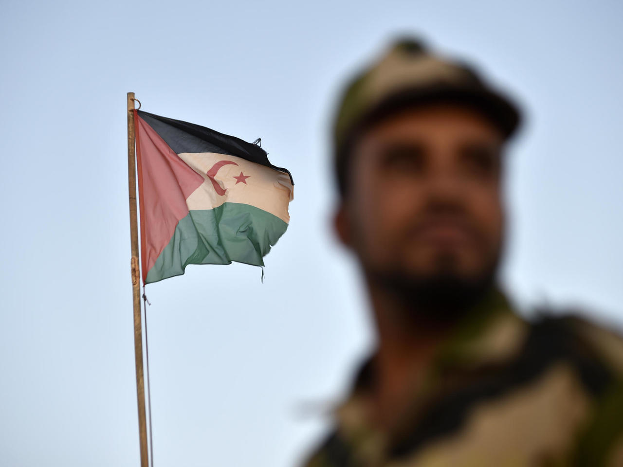 A Polisario Front soldier stands before a Sahrawi flag in Western Algeria