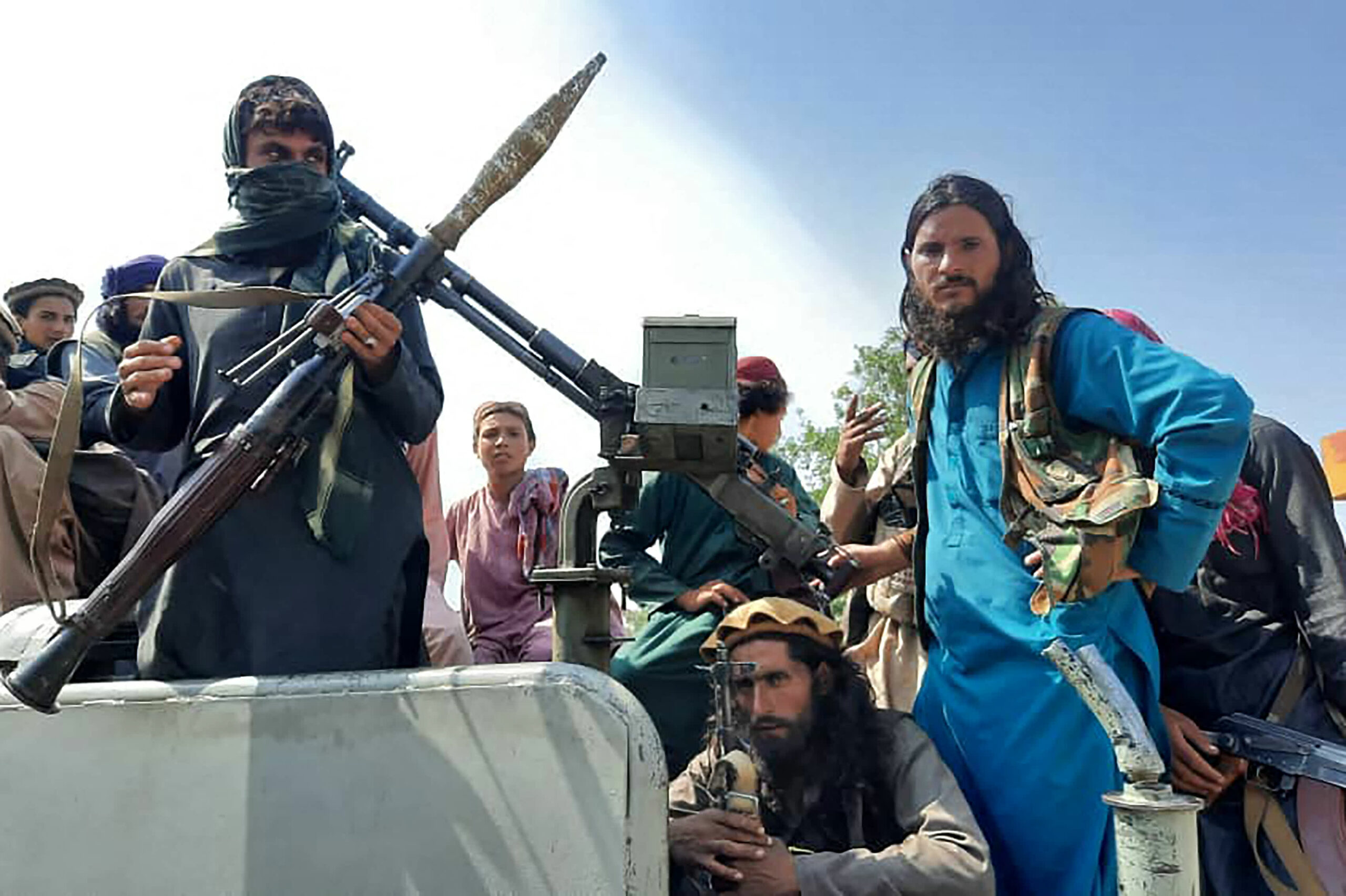 Taliban fighters sit over a vehicle on a street in Laghman province