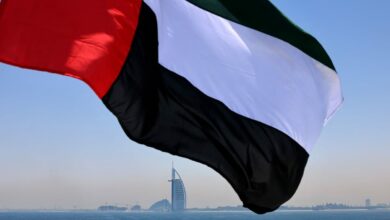 An Emirati flag fluttering above Dubai's marina with the Burj Al Arab landmark hotel in the background