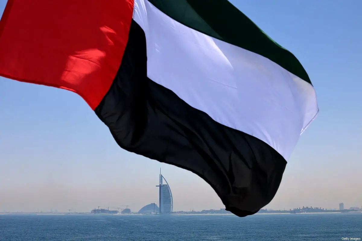 An Emirati flag fluttering above Dubai's marina with the Burj Al Arab landmark hotel in the background