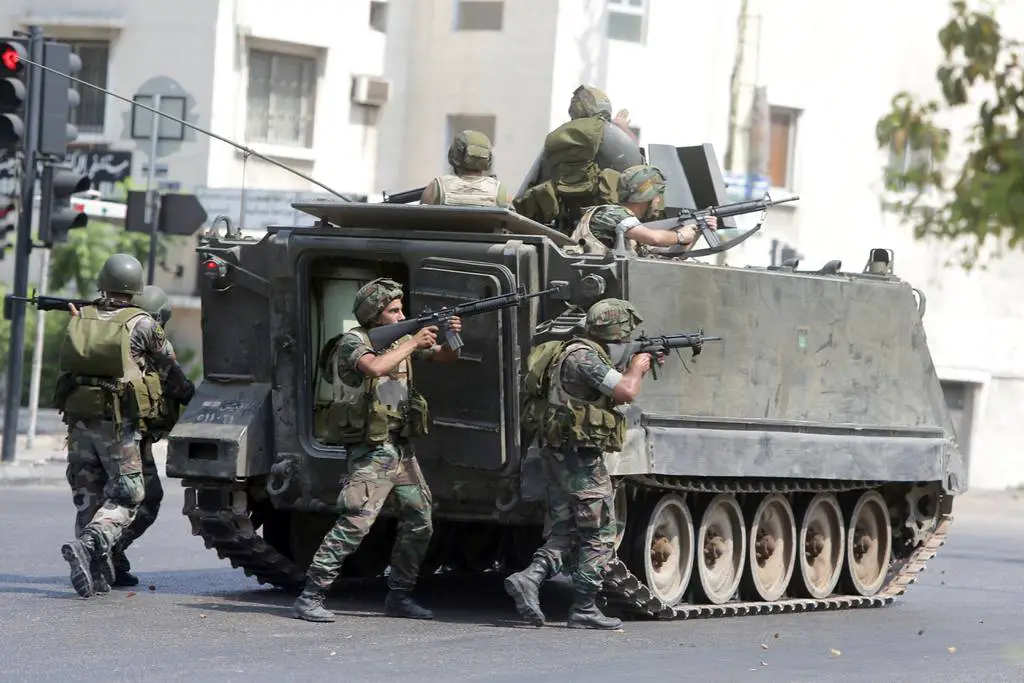 Lebanese soldiers take cover behind their armored vehicle as they enter the Abra neighborhood on the eastern outskirts of Sidon
