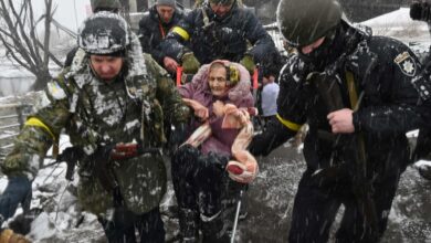 Ukrainian soldiers help an elderly woman to cross a destroyed bridge