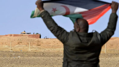 A Saharawi man holds up a Polisario Front flag near Moroccan soldiers guarding the wall separating the Polisario controlled Western Sahara from Morocco