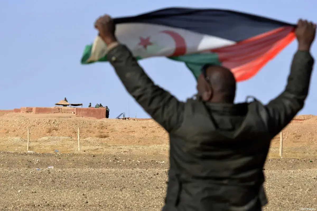 A Saharawi man holds up a Polisario Front flag near Moroccan soldiers guarding the wall separating the Polisario controlled Western Sahara from Morocco
