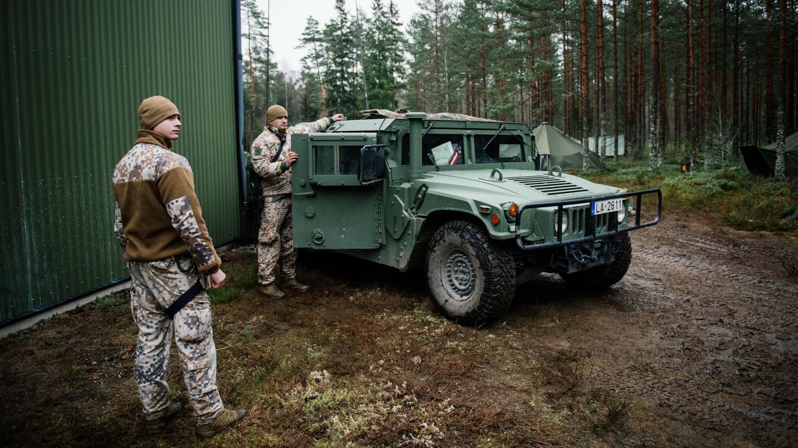 Soldiers from the Latvian National Armed Forces stand next to an armored Hummer vehicle