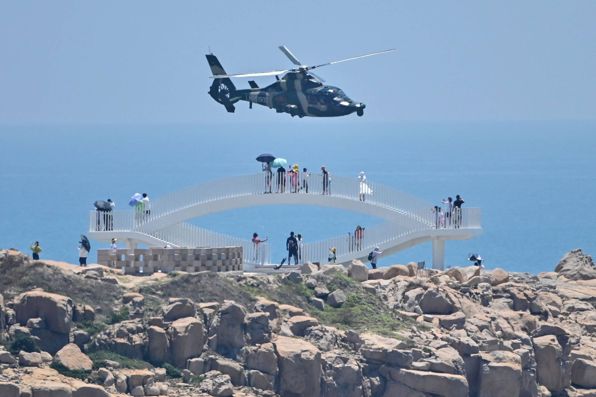 Tourists look on as a Chinese military helicopter flies past Pingtan island, one of mainland China's closest points to Taiwan, in Fujian province on Thursday, ahead of massive military drills off Taiwan