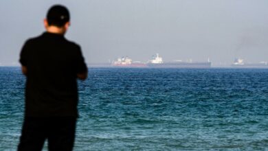 A man stands on a beach as tanker ships are seen in the waters of the Gulf of Oman