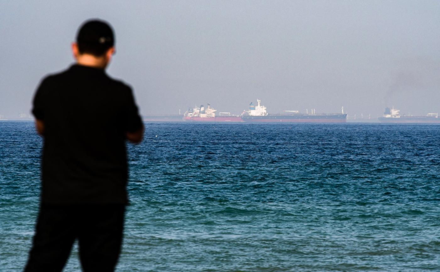 A man stands on a beach as tanker ships are seen in the waters of the Gulf of Oman