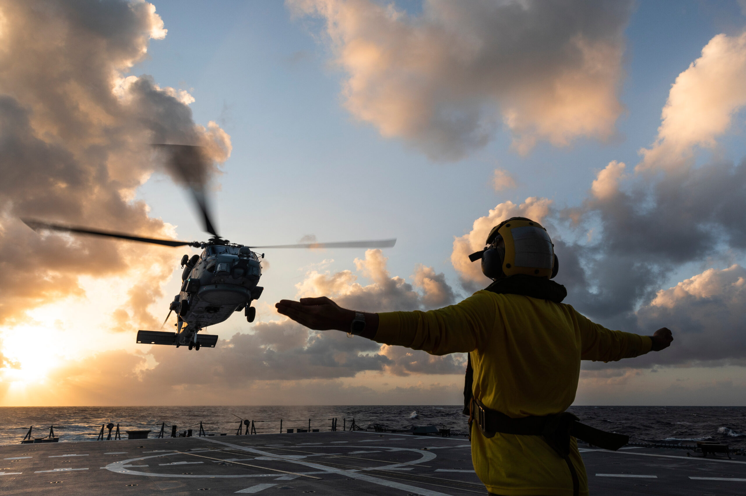 MH-60R helicopter landing on HMAS Hobart at sunset.