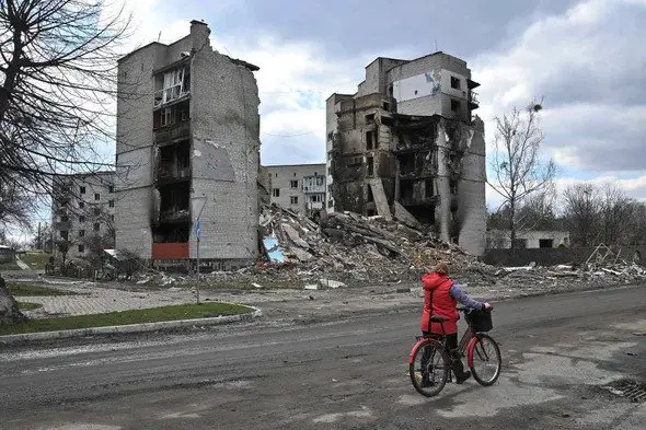 A woman carries her bicycle past destroyed buildings in the town of Borodianka, northwest of Kyiv