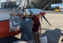 Engineers from the Naval Air Warfare Center Aircraft Division apply a fiducial tag aboard a T-6 Texan to autonomously capture arrival and departure data during ground operations in an experiment at Naval Air Station Patuxent River, Maryland in 2022. (U.S. Navy photo)