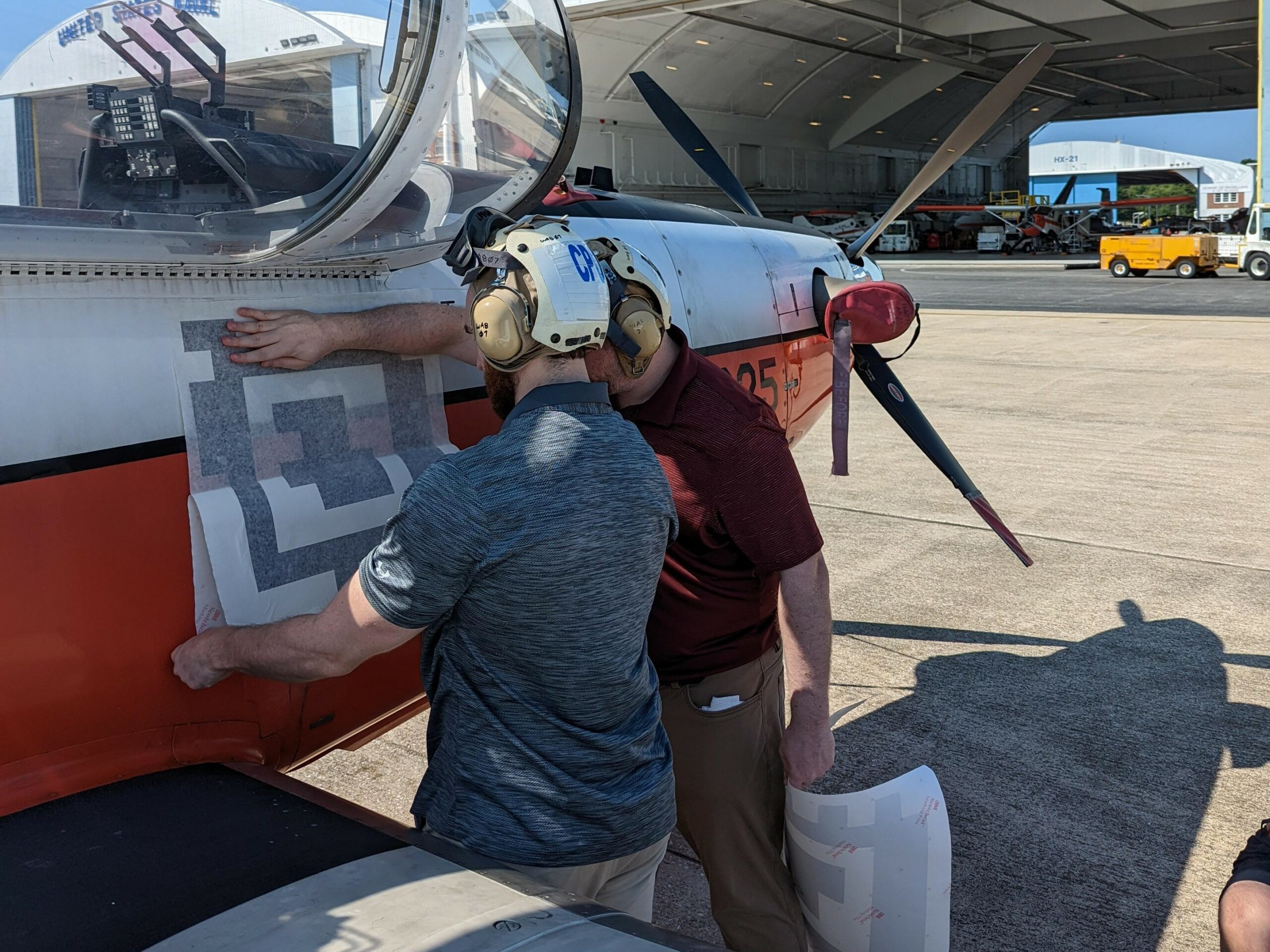 Engineers from the Naval Air Warfare Center Aircraft Division apply a fiducial tag aboard a T-6 Texan to autonomously capture arrival and departure data during ground operations in an experiment at Naval Air Station Patuxent River, Maryland in 2022. (U.S. Navy photo)
