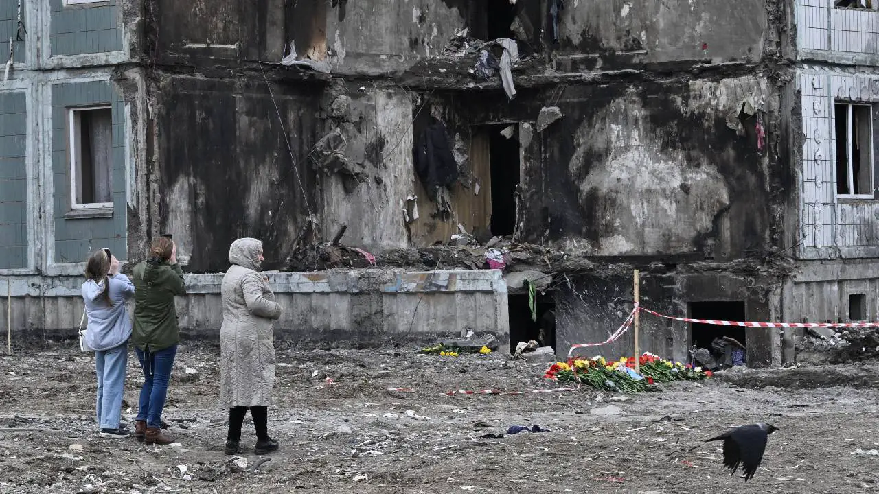 People pay their respects in front of a damaged multistory residential building