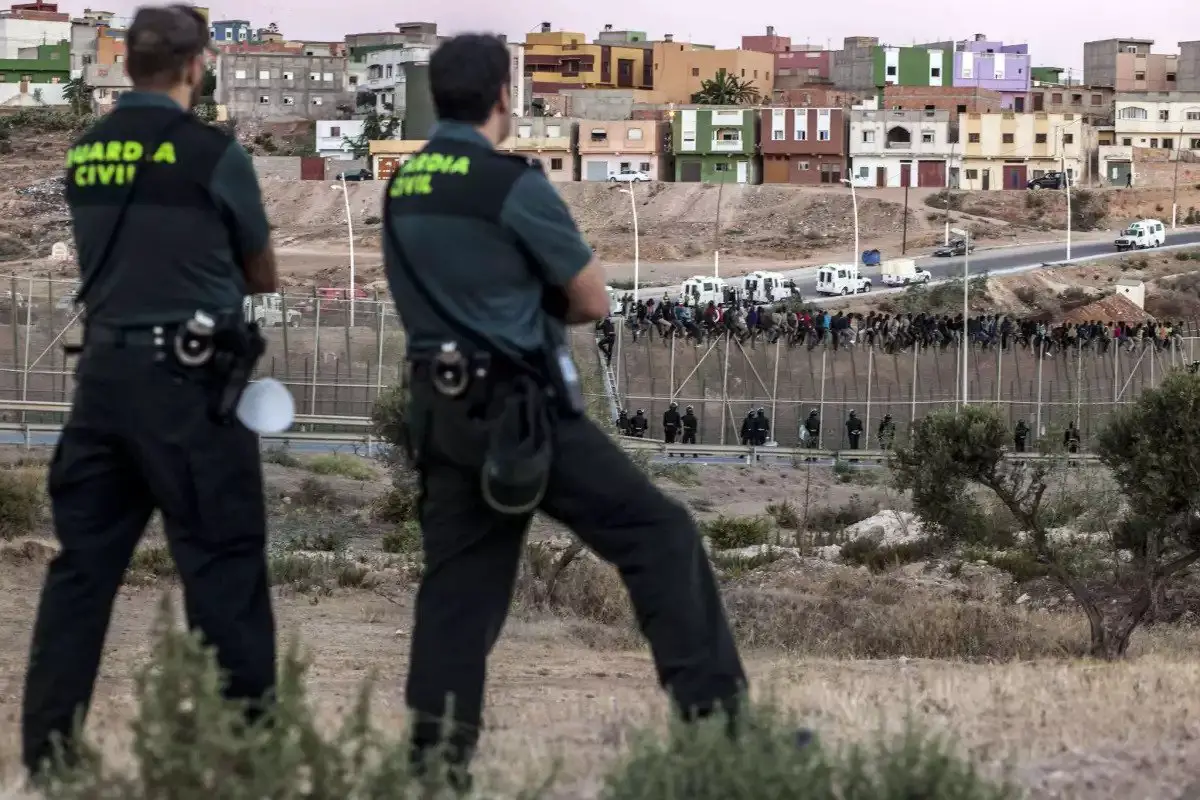 Spanish Guardia Civil watch as would-be immigrants from Africa sit atop a fence after scrambling over two other border barriers on Spain’s tiny north African territory of Melilla