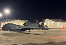 NATO's Northrop Grumman RQ-4D drone is seen on a landing area at night. The location is lit up by overhead lights.