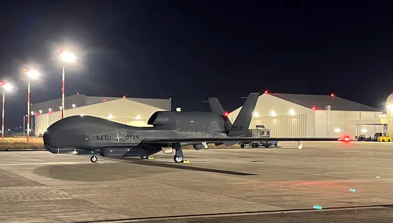 NATO's Northrop Grumman RQ-4D drone is seen on a landing area at night. The location is lit up by overhead lights.