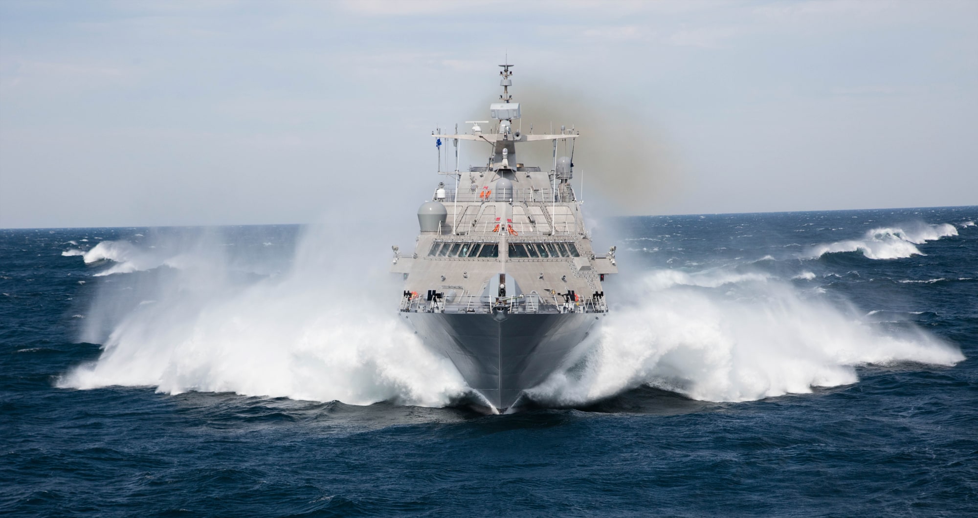 USS Milwaukee (LCS-5) sets sail in open waters. It sprays ocean water mist from its sides as it moves forward.