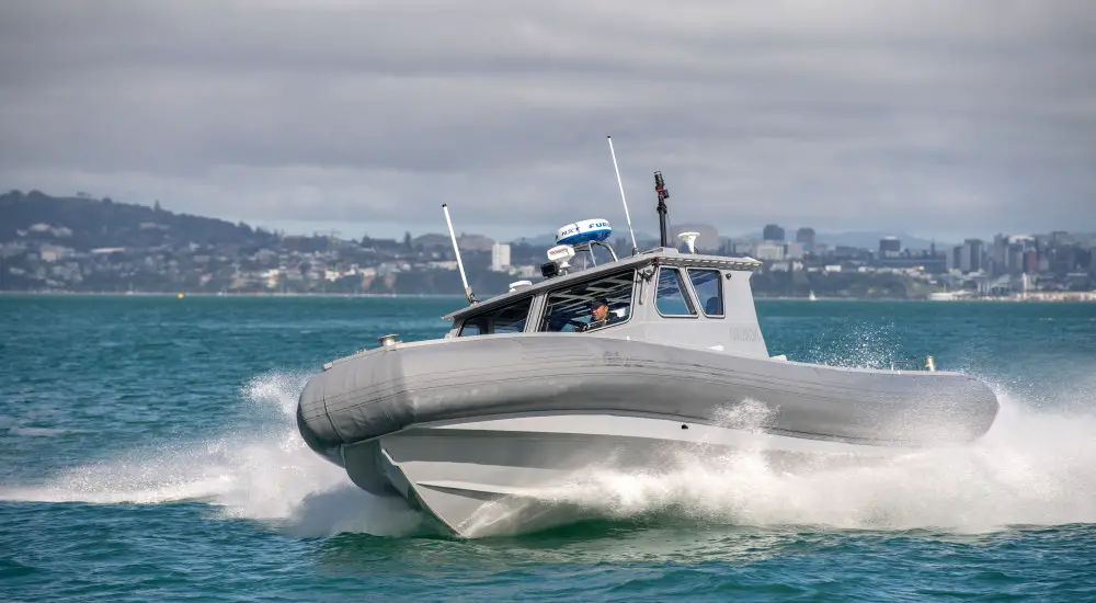 A Royal New Zealand Navy Littoral Manoeuvre Craft boat is seen gliding across the waters. A mountainside is seen in the back.