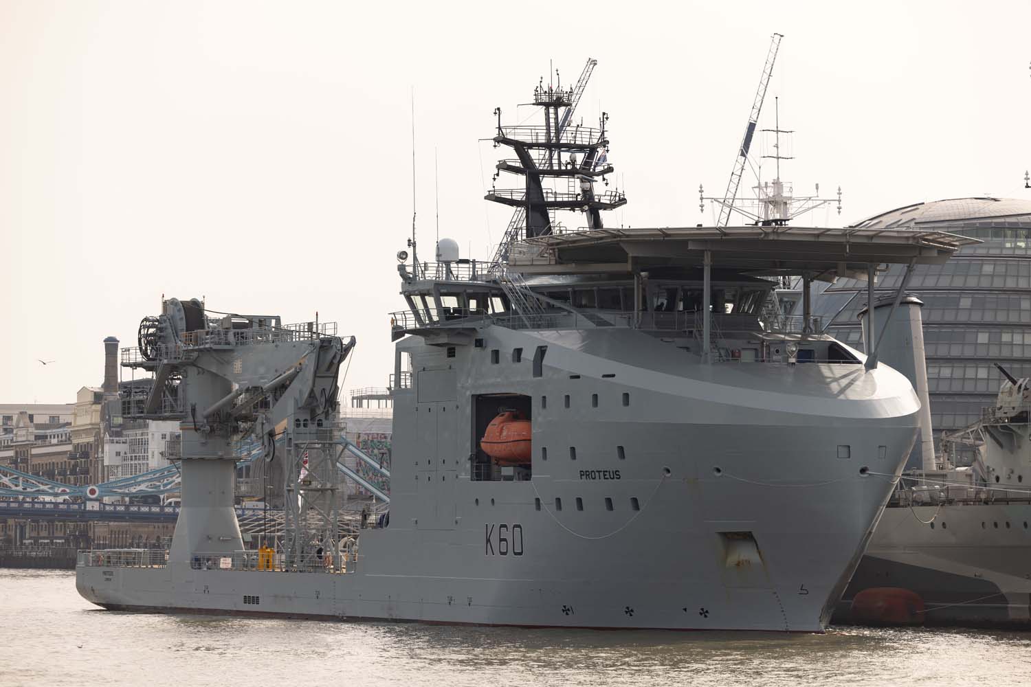 RFA Proteus is seen docked in London. HMS Belfast, an old UK wartime ship, is seen in the background beside Proteus.