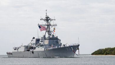 USS Chung-Hoon (DDG 93) is seen docked near a sandy shore. Its hull is painted in grey.