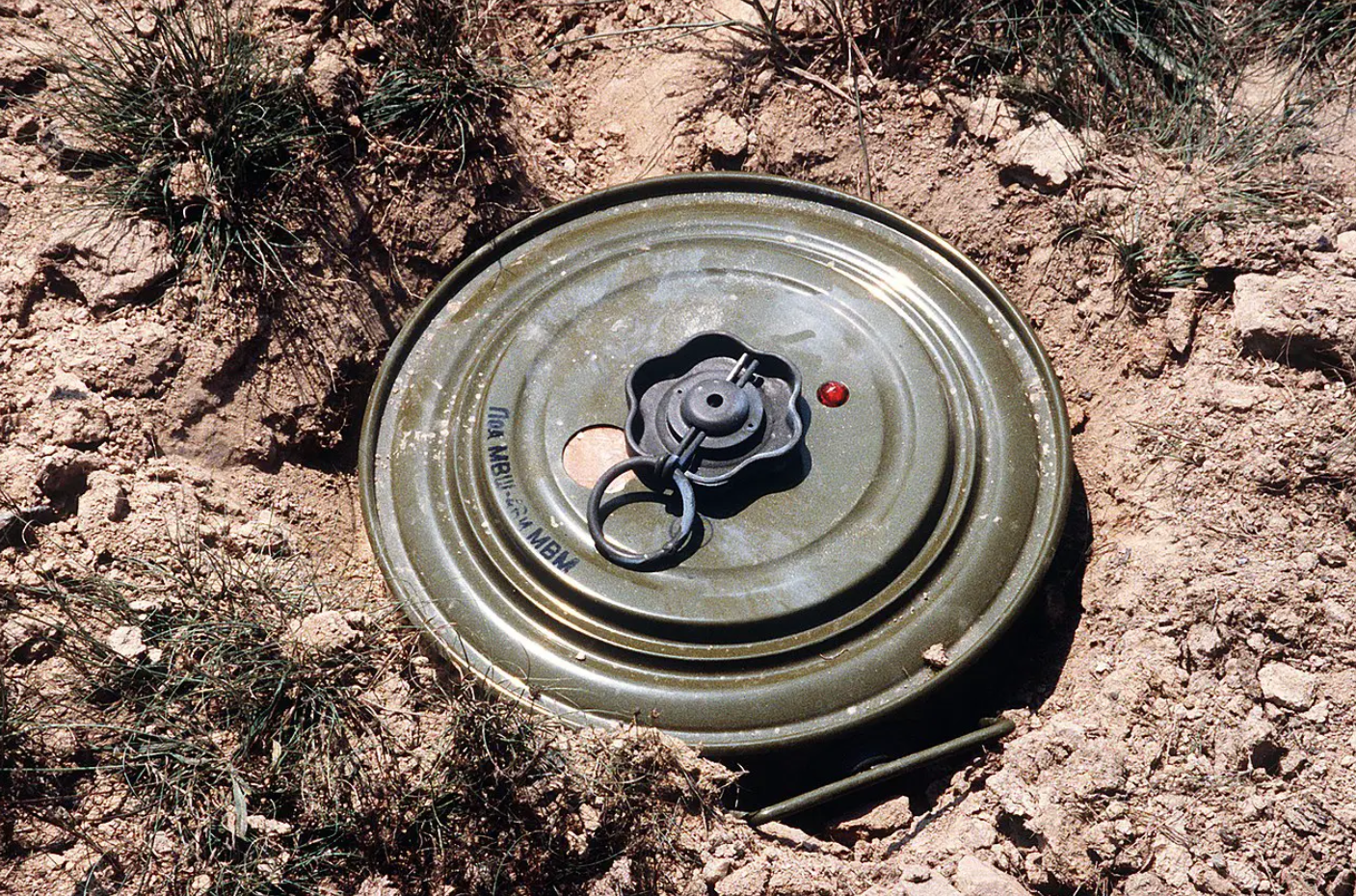 A Russian tank mine is seen on the ground. It is surrounded by dirt, seemingly before being buried.