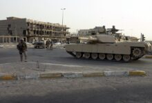 An M1A1 Abrams tank provides area security alongside a street intersection beside Marines during a 2005 operation in Fallujah, Iraq