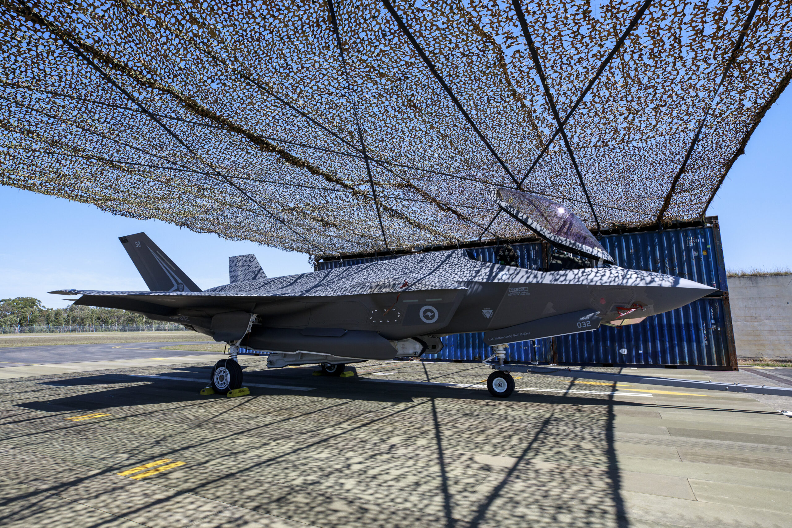 An F-35A Lightning II aircraft under a temporary aircraft revetment being trialled at RAAF Base Williamtown, New South Wales. *** Local Caption *** In October 2023, the Air Combat Group initiated and executed a trial to construct a temporary aircraft revetment at RAAF Base Williamtown. The trial demonstrated alternative passive defence methods and materials. Aircraft revetments are open-air structures intended to shield parked aircraft from discovery, blast and fragmentation damage. Personnel from No.65 Air Base Recovery Squadron were tasked with constructing the revetment. The trial aimed to inform Air Force of future dispersed aircraft revetment solutions in support of agile operation concepts.