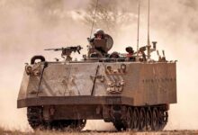An Israeli army armored tracked vehicle moves near a stationed artillery howitzer at a position along the border with the Gaza Strip in southern Israel