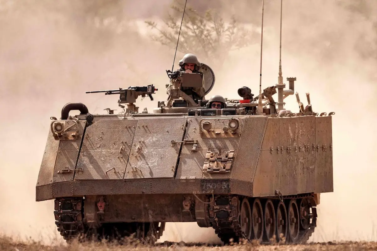 An Israeli army armored tracked vehicle moves near a stationed artillery howitzer at a position along the border with the Gaza Strip in southern Israel