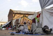 Men sit and lie outside tents and shelters pitched at the Hasahisa secondary school on July 10, 2023, which has been made into a make-shift camp to house the internally displaced fleeing violence in war-torn Sudan