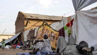 Men sit and lie outside tents and shelters pitched at the Hasahisa secondary school on July 10, 2023, which has been made into a make-shift camp to house the internally displaced fleeing violence in war-torn Sudan