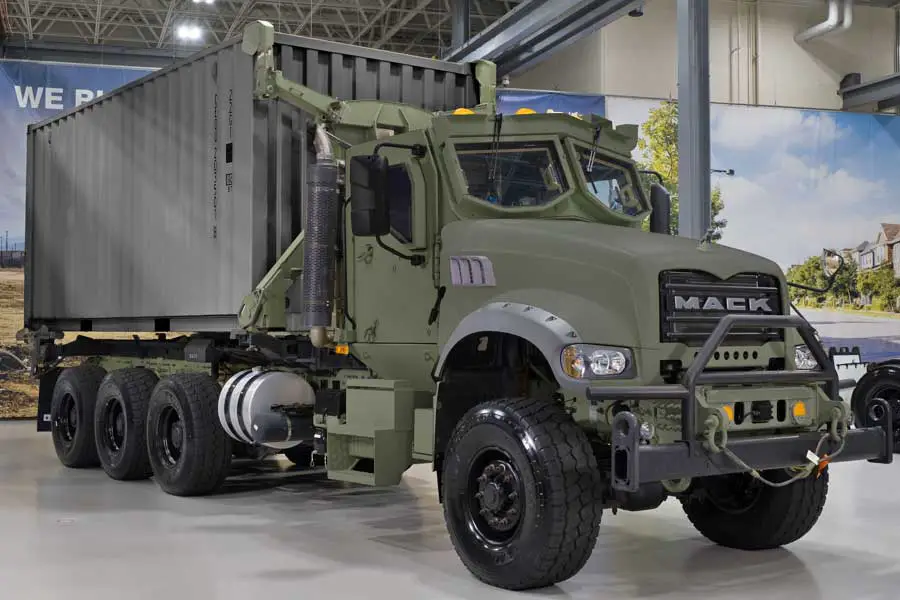A Mack truck is seen on display at what appears to be a warehouse. It's colored dark green and has the 'MACK' logo in front of the truck.