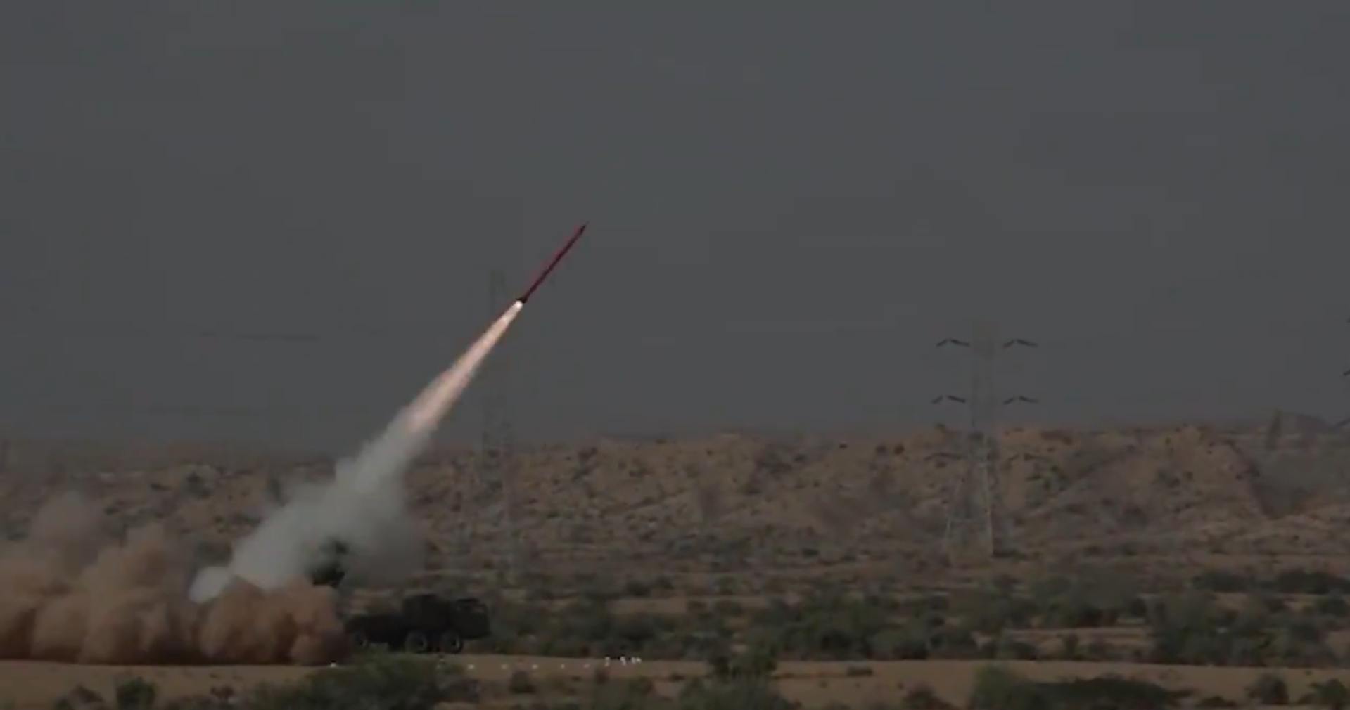 A Fatah-II missile is launched in a plains. It's seen blasting off to the northeast. The plains have green bushes scattered across its yellow sands.