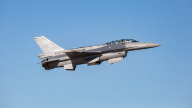 A gray Lockheed Martin F-16 jet plane is seen flying in clear blue skies. It has "1101" painted at the back, below its tail.
