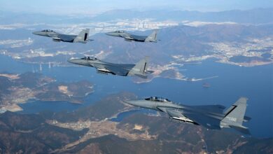 Four gray Republic of Korea Air Force fighter jets are seen flying high above a landscape with a wide, winding river passing through it.