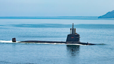The black Humaitá (S-41) submarine is seen breaking the surface of the sea. Near the top of its hatch, "S-41" is painted in red. The sea and the sky are a calm blue.