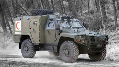 An Otokar Cobra II armored vehicle is seen driving around on a snowy forested area. Its green-gray paint blend in well with the environment.
