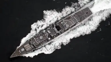 A UK Royal Navy ship is seen sailing deep dark-blue waters. The scene is shown from a top-down view.