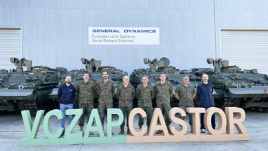 Six uniformed Spanish Army personnel stand in front of four ASCOD Castor armored combat vehicles. They are joined by two civilians, likely from General Dynamics. In front of them are letter standees that spell out "VCZAP CASTOR". The background is a warehouse building, with a sign that reads "GENERAL DYNAMICS European Land Systems Santa Barbara Sistemas".