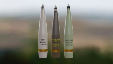 Three Rheinmetall 155mm ER021A ammunition are lined up and propped up. They are colored white, brown, and green, respectively.