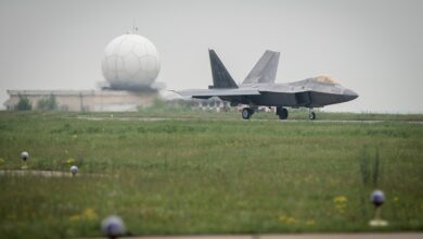 A gray F-22A Raptor jet plane taxis at Mihail Kogalniceanu Airport, with a globe-shaped radar station radome visible in the background.