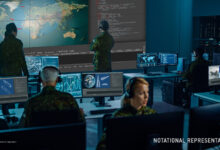 Notational representation of the Command and Control, Battle Management and Communications (C2BMC) system. Four soldiers are seen stationed in front of computers in desks. The computer screens display various kinds of graphs and figures. Two soldiers in the back are checking out similar graphs seen displayed on screens installed on the wall.