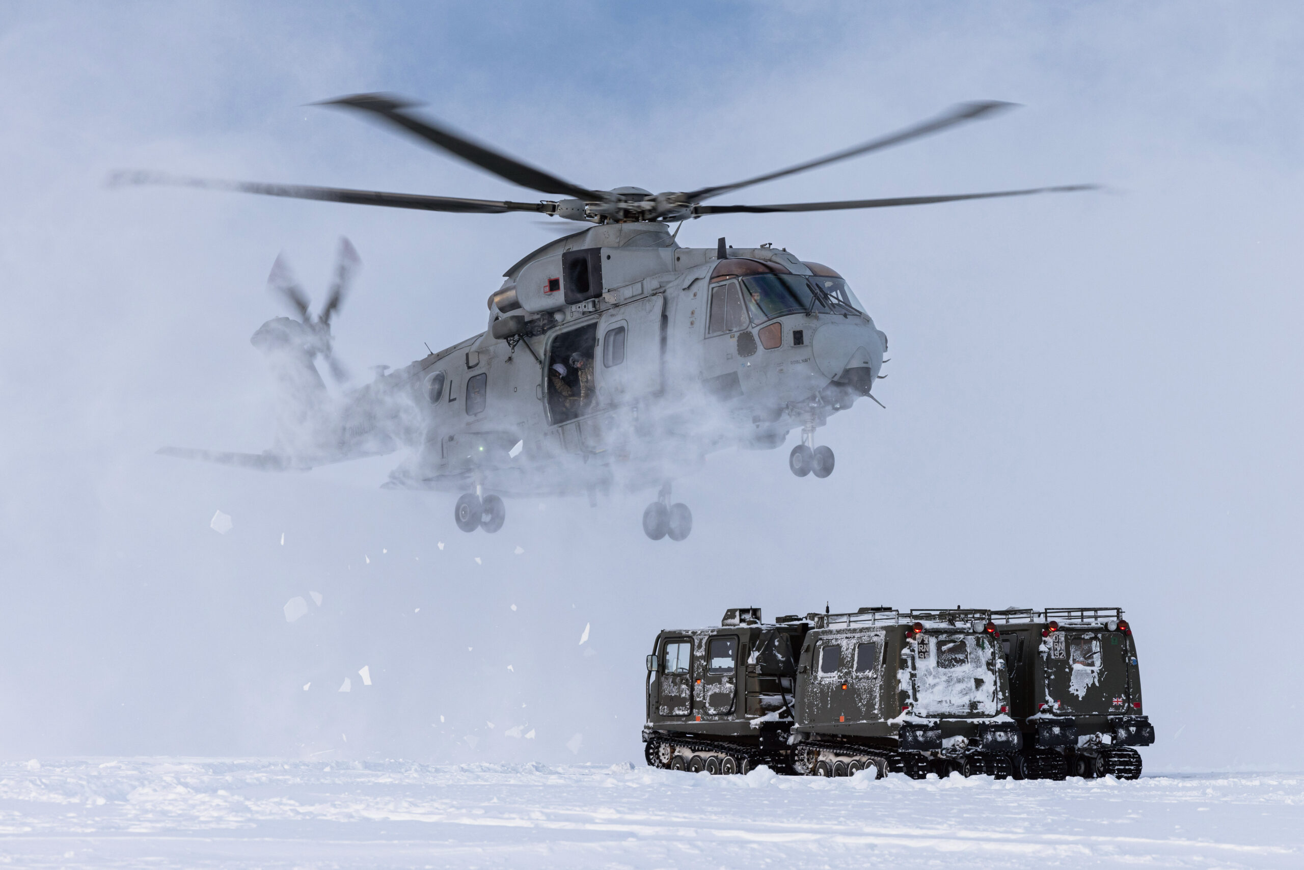 Pictured: A Merlin Mk4 of 845 NAS performs a snow landing using MAOTS BV Vehicles as reference. 845 NAS and CDO MOAT TRAIN WITH RN MEDICS IN ARCTIC ENVIRONMENT. 845 Naval Air Squadron (NAS) and the Commando Mobile Air Operation Team (Cdo MAOT) have conducted training with the Medical Squadron of Commando Logistic Regiment. The objective of the training was to teach the attached Royal Marines, Royal Navy Medical Assistants, Naval Nurses, and Medical Officers of the Forward Surgical Teams (FSTs) and as a group, known as the Commando Forward Surgical Group (CFSG) in Stage 1 Evacuation drills from the Merlin Mk4 and Arctic Casualty Loading Drills in the field. As the CFSG team were dropped off by 845 NAS, Cdo MAOT assisted by the MAOT team of the Joint Helicopter Support Squadron (JHSS) took over the training by first getting them into a ‘Arctic Huddle’ to protect themselves from the freezing downwash of the merlin as they took back off. The CFSG were then shown how to assess suitable Helicopter Landing Sites in deep snow and frozen areas. Op CLOCKWORK (Formally Exercise CLOCKWORK) has been running at Bardufoss for over 50 years and delivers Environmental Flying Qualifications, Cold Weather Survival, Tent Group Commanders and Snow and Ice driving courses to ensure that the personnel of the Joint Helicopter Command (JHC) are trained to operate in the harshest of environments.