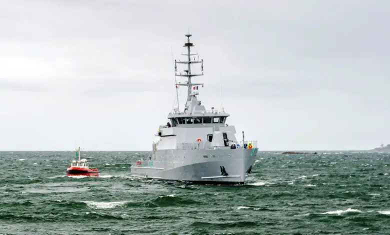 Cayor, a 58 S-class offshore patrol vehicle, is seen sailing in green-blue waters. The gray seacraft is accompanied by a much smaller red boat, which is sailing on its right side.