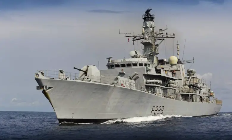 UK's HMS Lancaster warship is seen sailing deep blue waters. The gray ship has "F229" painted on its side in black. The background is a dull blue sky covered by dark clouds.